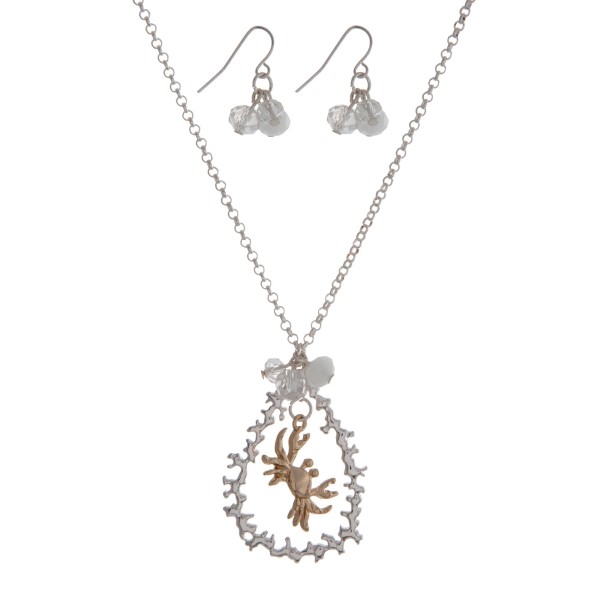 Silver tone necklace set with a two tone crab and coral reef teardrop pendant, accented with a white opal bead. Approximately 18" in length. 