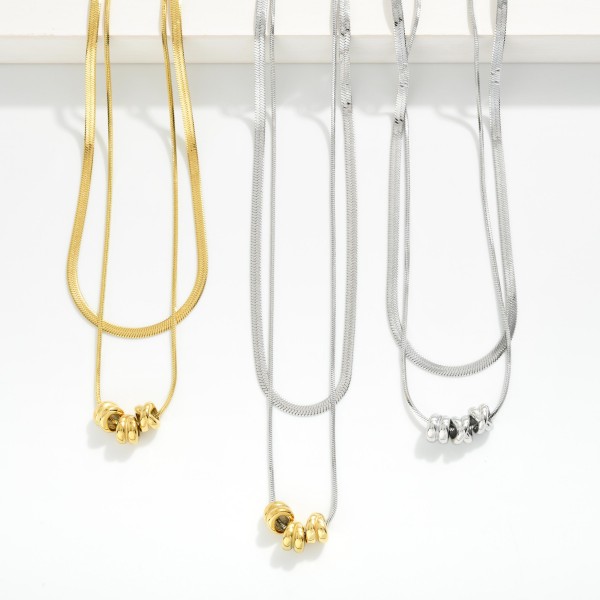 Layered Herringbone Chain Link Necklace Feating Metal Tone Beaded Disks 

- Stainless Steel 
- Approximately 16.5" L
- Extender 2" L 