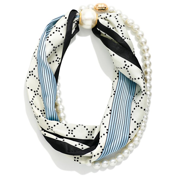 Satin Scarf and Pearl Necklace that twists a silky scarf in lattice and pinstripe prints together with a strand of faux pearls, finished with an oversized pearl closure. The blend of soft fabric and classic pearls creates an effortless, Parisian inspired look in seconds. Wear it with a crew neck sweater, button down, or simple dress to instantly finish an outfit. A unique, giftable accessory that stands out on the display and appeals to shoppers who love an easy, styled look.