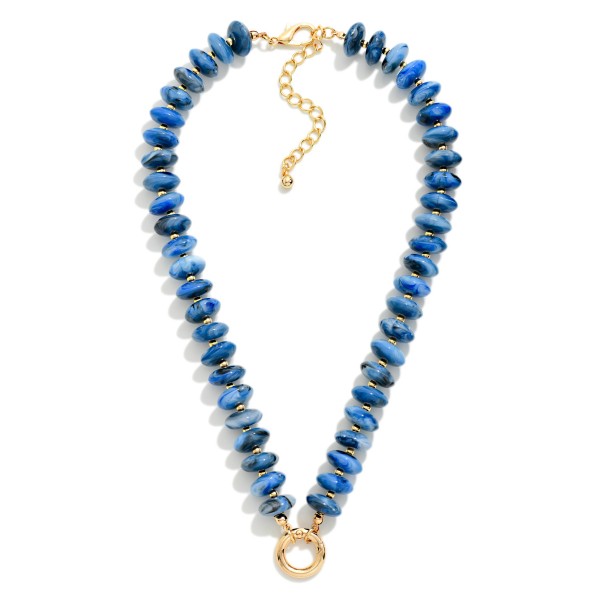 Rondelle Bead Necklace lined with glossy marbled beads that taper into a V shape and finish with a polished open ring accent at the center. The streamlined design sits beautifully at the neckline and layers easily with chains and pendants. Wear it with open collars, V neck tops, and simple knits for an instant pop of texture. A trend right beaded style at an approachable price, it is an easy one to stock deep for the season.