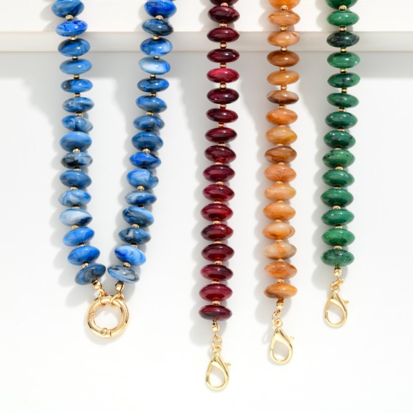 Rondelle Bead Necklace lined with glossy marbled beads that taper into a V shape and finish with a polished open ring accent at the center. The streamlined design sits beautifully at the neckline and layers easily with chains and pendants. Wear it with open collars, V neck tops, and simple knits for an instant pop of texture. A trend right beaded style at an approachable price, it is an easy one to stock deep for the season.