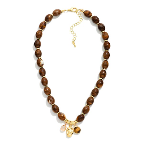 Polished Oval Bead Necklace with a cluster of mixed charms at the center, including a smooth stone drop and a hammered metal disc. The glossy beads have a natural, stone inspired finish that adds warmth to fall and winter outfits. A lobster clasp and extender chain make sizing simple. Charm accents give this style a personal, collected feel that shoppers love, making it an easy gift and a dependable seller.