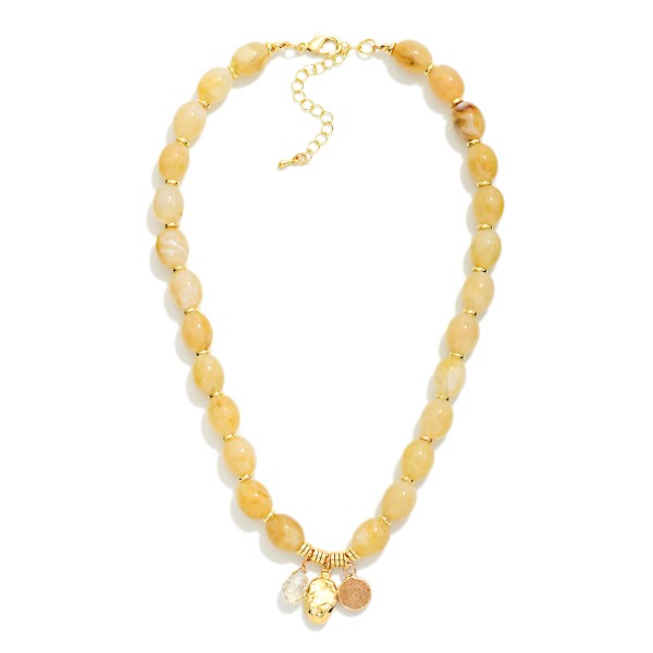 Polished Oval Bead Necklace with a cluster of mixed charms at the center, including a smooth stone drop and a hammered metal disc. The glossy beads have a natural, stone inspired finish that adds warmth to fall and winter outfits. A lobster clasp and extender chain make sizing simple. Charm accents give this style a personal, collected feel that shoppers love, making it an easy gift and a dependable seller.