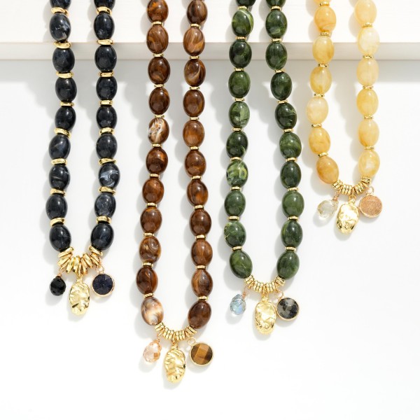 Polished Oval Bead Necklace with a cluster of mixed charms at the center, including a smooth stone drop and a hammered metal disc. The glossy beads have a natural, stone inspired finish that adds warmth to fall and winter outfits. A lobster clasp and extender chain make sizing simple. Charm accents give this style a personal, collected feel that shoppers love, making it an easy gift and a dependable seller.