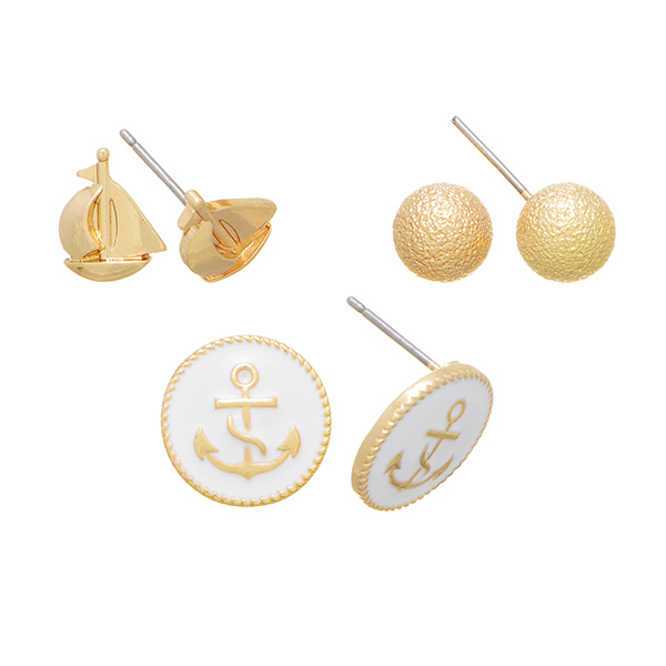 Gold tone set of three post earrings featuring a textured ball, metal sailboat, and an anchor with white enamel background.