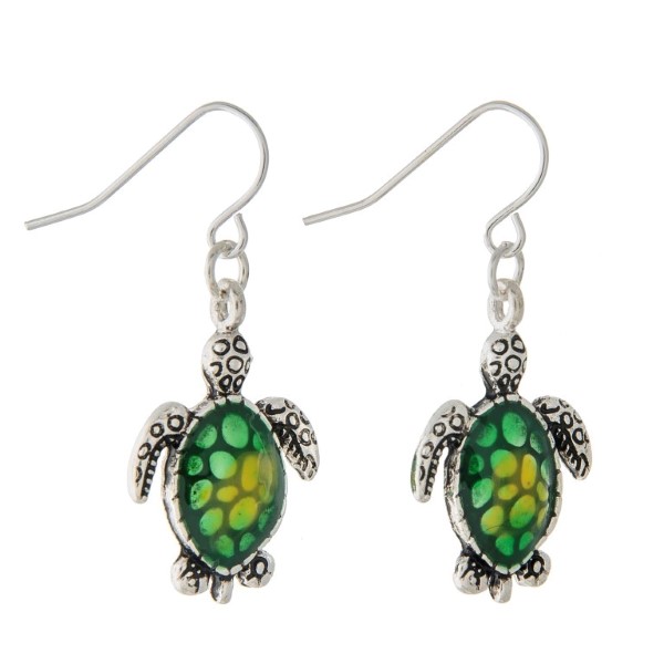 1 1/4" Silver tone fishhook style earrings featuring a small sea turtle shaped design accented by a green ombre style shell.