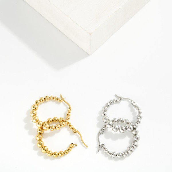 Metal Tone Beaded Huggie Hoop Drop Earring 

- Approximately 1" D 
- Stainless Steel 
- Water Resistant 
- Hypoallergenic