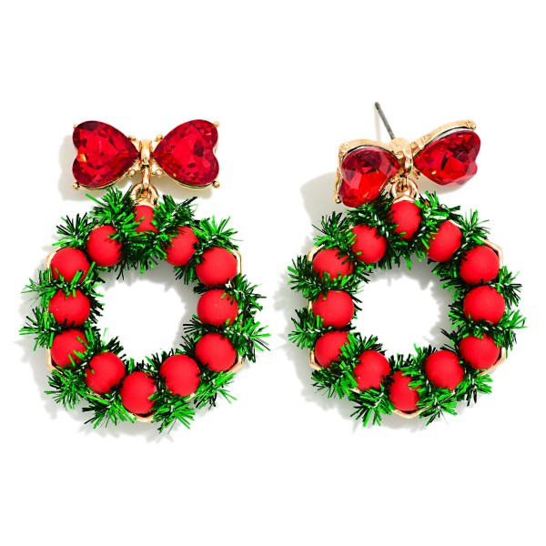 Tinsel Wreath Drop Earrings featuring a fluffy tinsel garland wreath dotted with round berry beads, hanging from a heart cut crystal bow post. The textured tinsel gives a soft, dimensional look that feels just like a real holiday wreath. A festive favorite for Christmas parties, tree trimming nights, and holiday markets. Playful and full of texture, wreath earrings are a classic seasonal seller that customers snap up in November and December.