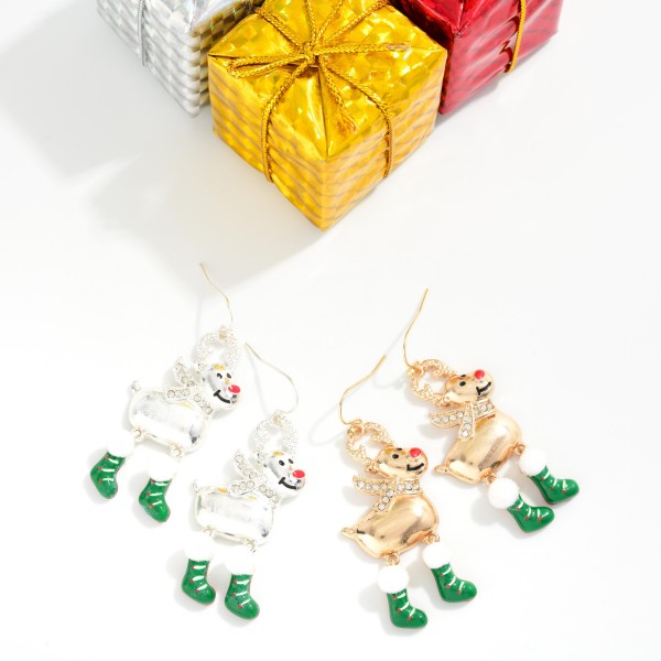 Rhinestone Reindeer Stocking Drop Earrings featuring a cheerful reindeer with sparkling rhinestone antlers and scarf, a shiny button nose, and dangling enamel stocking legs topped with fluffy pom trim. The movable stocking charms swing with every step for a playful, festive look on lightweight fishhook wires. A crowd pleaser for Christmas parties, school events, and holiday photos. Whimsical character earrings like these are top holiday impulse buys.