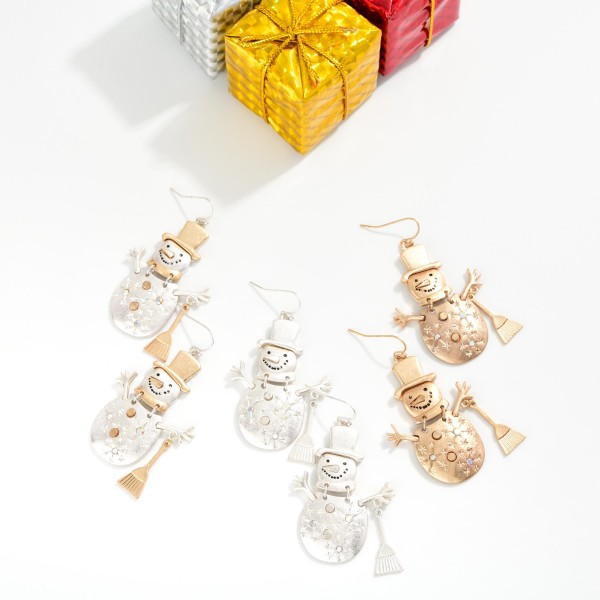 Vintage Metal Snowman Drop Earrings featuring a jolly snowman in a top hat with stick arms, a tiny broom, and etched snowflake details, all in a worn, burnished metal finish. Lightweight fishhook wires keep them comfortable for all day wear. Perfect for winter festivals, classroom parties, and holiday gift exchanges. Whimsical, rustic, and priced right, these are an easy seasonal add on that sells from November through January.
