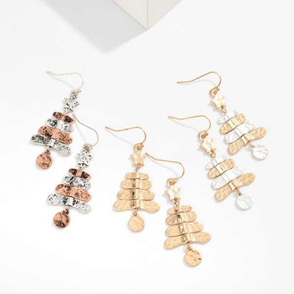 Hammered Metal Christmas Tree Drop Earrings featuring stacked, hammered tiers topped with a tiny star and finished with a dangling round ornament charm. The worn, burnished finish gives a rustic, vintage feel that pairs perfectly with sweaters, flannels, and boots. A charming pick for farmhouse and western boutiques, holiday markets, and gift exchanges. Lightweight on fishhook wires, these sell easily as stocking stuffers and impulse adds.