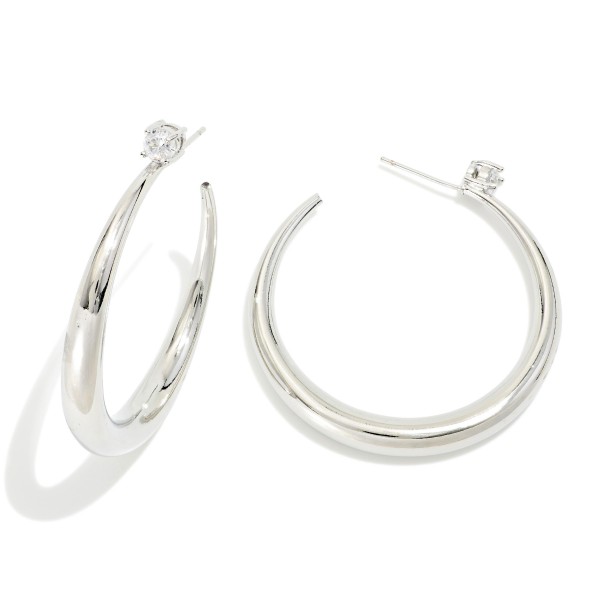 Tapered Open Hoop Earrings with a graduated, sculpted profile that thickens toward the bottom for a modern, polished look. A tiny sparkling stone accents each post for a subtle touch of shine. Easy to dress up or down for work, weekends, and special events. Sleek statement hoops like these are a boutique staple that sells consistently all year.