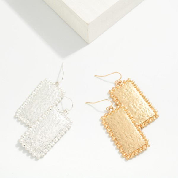 Hammered Rectangle Drop Earrings with a textured metal panel framed by a beaded ball edge on fishhook wires. The shimmer of the hammered surface paired with the dotted trim gives a vintage inspired look that stays light enough for daily wear. Easy to pair with everything from tees to holiday dresses. A dependable metal drop that sells to every age at an easy price.