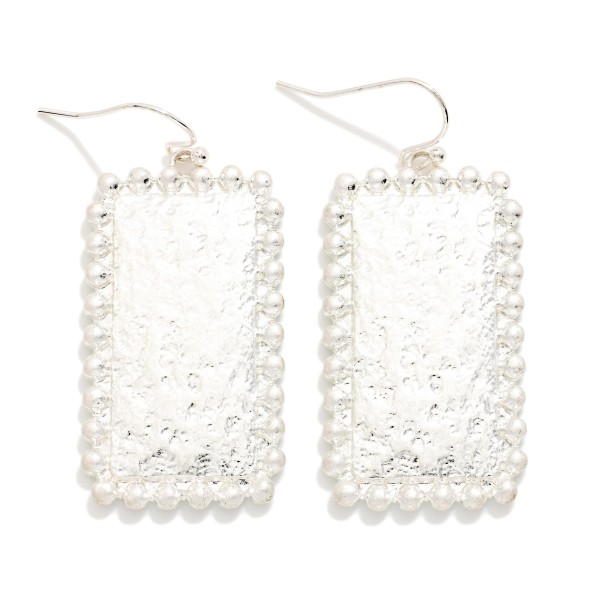 Hammered Rectangle Drop Earrings with a textured metal panel framed by a beaded ball edge on fishhook wires. The shimmer of the hammered surface paired with the dotted trim gives a vintage inspired look that stays light enough for daily wear. Easy to pair with everything from tees to holiday dresses. A dependable metal drop that sells to every age at an easy price.
