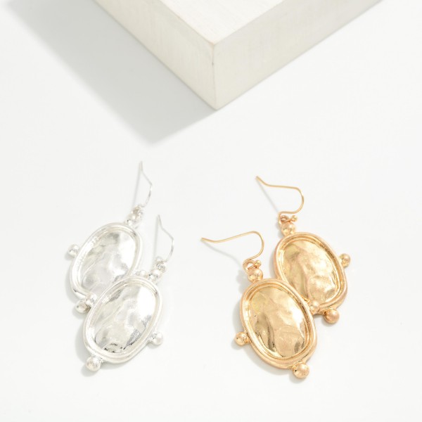 Hammered Oval Drop Earrings with a polished framed medallion accented by tiny ball details on fishhook wires. The hammered center reflects light like a mirror for a vintage inspired look that stays lightweight. An easy everyday style for workwear, church and weekend outfits. A classic metal drop at an easy price point that works for every age.