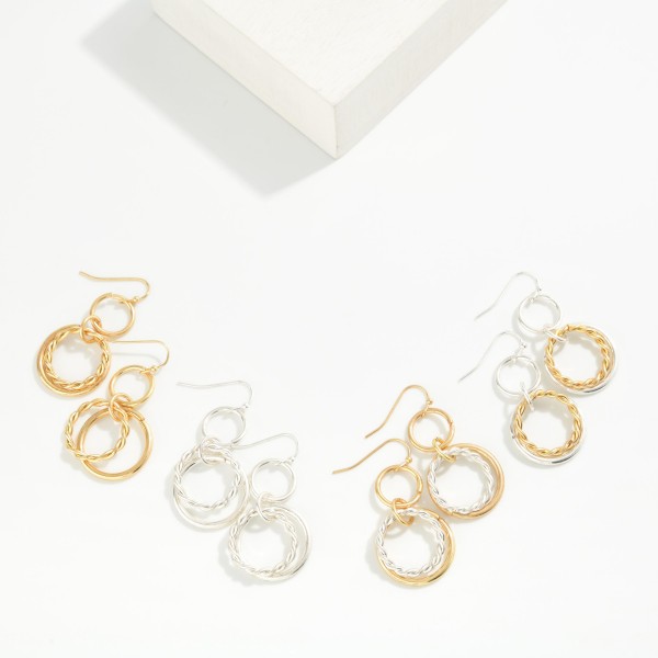 Twisted Rope Double Hoop Drop Earrings featuring a smooth open ring paired with a twisted rope hoop, suspended from a small circle link on fishhook wires. The layered texture adds dimension and movement without extra weight. Easy to wear from day to night. Offered in mixed and single metal finishes, they make a versatile everyday style that sells across a wide range of customers.