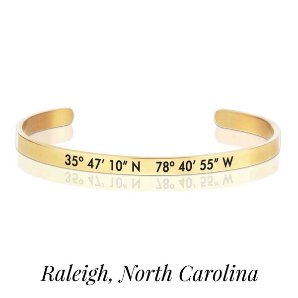 Gold tone cuff bracelet stamped with the coordinates of Raleigh, North Carolina. 