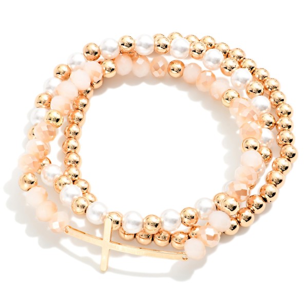 Sideways Cross Beaded Bracelet Set featuring coordinated strands of faceted glass beads, faux pearls, and polished metal beads, anchored by an east west cross centerpiece. Wear the full stack for impact or split the strands for a lighter look. Stretch fit for easy on and off. A popular faith style offered in several bead mixes, it's an easy gift for any occasion.