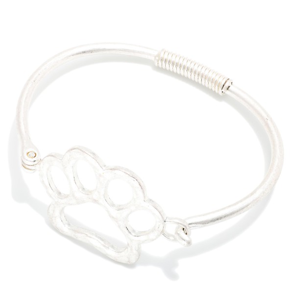 Paw Print Wire Bangle Bracelet featuring an open paw print design set into a slim wire band with a coiled wrap detail. The hook closure makes it easy to put on and take off. A sweet gift for pet lovers, animal rescue supporters, and school spirit fans with a paw mascot. Affordable and easy to stack, it's a fun impulse buy for any boutique.