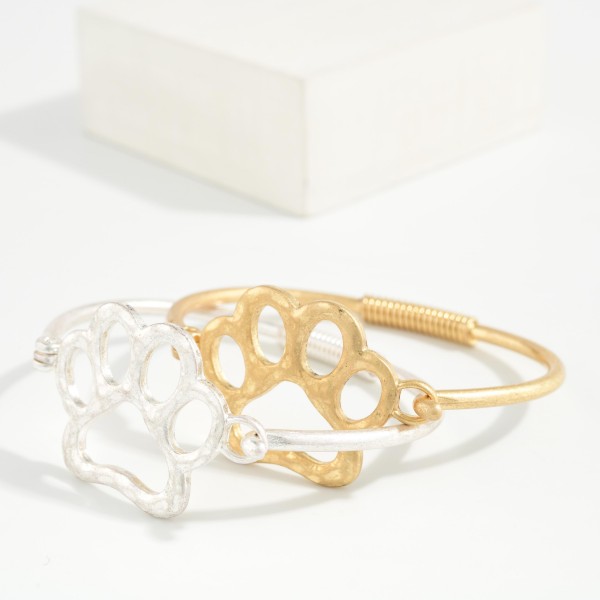 Paw Print Wire Bangle Bracelet featuring an open paw print design set into a slim wire band with a coiled wrap detail. The hook closure makes it easy to put on and take off. A sweet gift for pet lovers, animal rescue supporters, and school spirit fans with a paw mascot. Affordable and easy to stack, it's a fun impulse buy for any boutique.