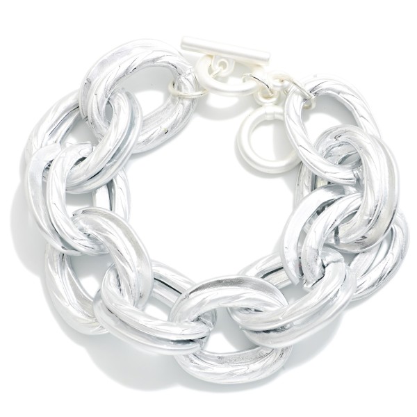Chunky Chain Link Toggle Bracelet featuring oversized oval links in a soft matte finish and a front toggle closure. Lightweight for its size, it delivers a bold look without weighing down the wrist. Pairs perfectly with the coordinating chunky chain necklace for a complete set. A trend favorite at an easy price point that sells quickly in boutiques.