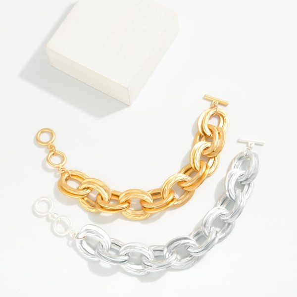 Chunky Chain Link Toggle Bracelet featuring oversized oval links in a soft matte finish and a front toggle closure. Lightweight for its size, it delivers a bold look without weighing down the wrist. Pairs perfectly with the coordinating chunky chain necklace for a complete set. A trend favorite at an easy price point that sells quickly in boutiques.