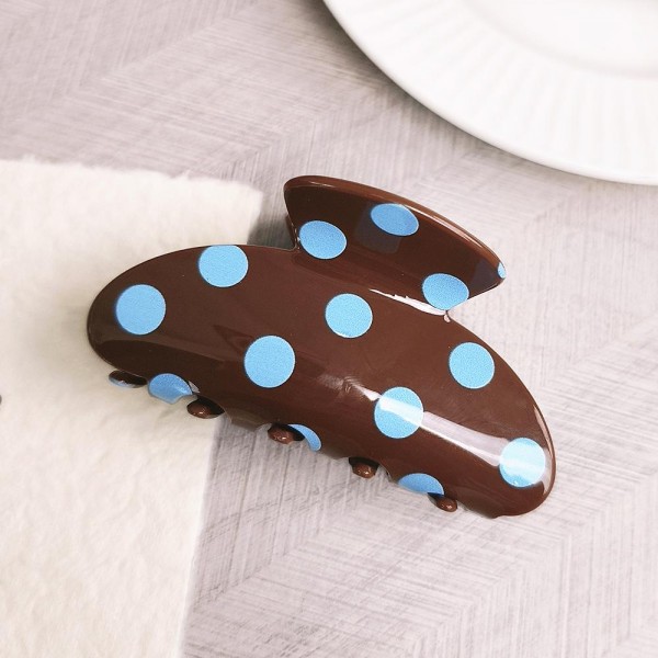 Polka dot claw hair clip in smooth acrylic with contrast painted dots and a mid-size profile. Strong-grip teeth hold a twist, a half-up, or a full clip-up on fine and thick hair alike without pulling or sliding out. Polka dots are a perennial retro print that pairs just as easily with denim and knits as with workwear. A steady everyday seller at an impulse price, and an easy multiple for customers building a clip collection.