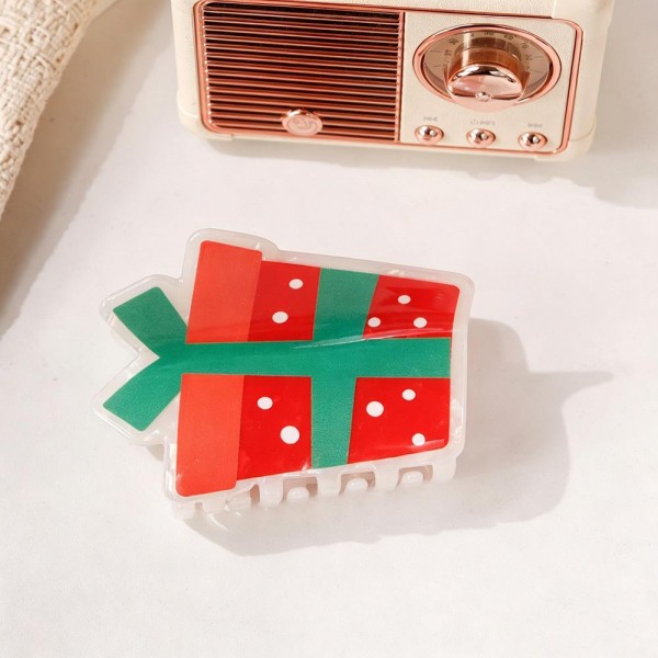 Wrapped gift box claw clip molded in glossy acrylic with a ribbon and bow detail across the front. The teeth hold a half up twist or a small bun without slipping, and the shape photographs beautifully against dark hair. A tiny piece of holiday styling that costs almost nothing to add to an order. Character clips like this sell through quickly once the December display goes up.