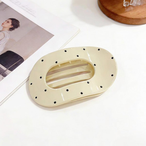 Oval hair barrette in a smooth acrylic finish with a scattered dot print and a hidden snap bar that clicks shut over a half up style or a low ponytail. The wide oval face covers the hardware, so the look stays clean from every angle. Comfortable enough to leave in through a full day at a desk. Statement barrettes finish a simple hairstyle in one step and sell steadily off a peg display.