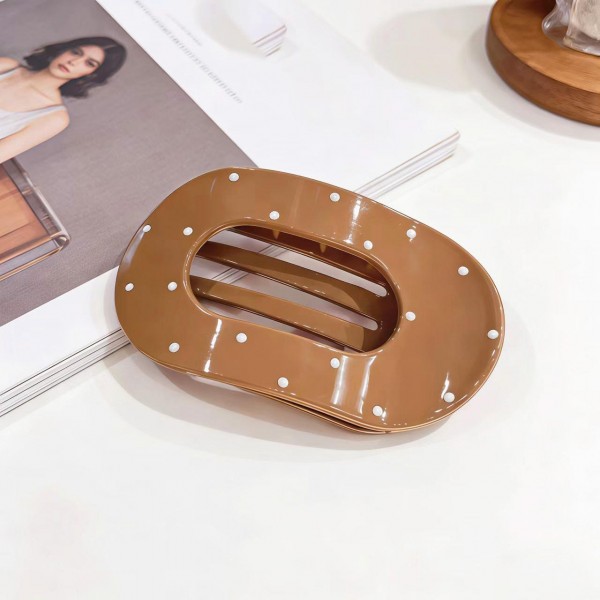 Oval hair barrette in a smooth acrylic finish with a scattered dot print and a hidden snap bar that clicks shut over a half up style or a low ponytail. The wide oval face covers the hardware, so the look stays clean from every angle. Comfortable enough to leave in through a full day at a desk. Statement barrettes finish a simple hairstyle in one step and sell steadily off a peg display.