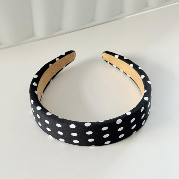 Padded headband with an allover polka dot print and a wide crown that holds hair back without pinching behind the ears. The firm band keeps its shape through a full day and the smooth finish will not snag fine hair. A retro print that dresses up a simple ponytail or a fresh blowout in one step. Headbands like this are a quick impulse add and they photograph beautifully on a display.
