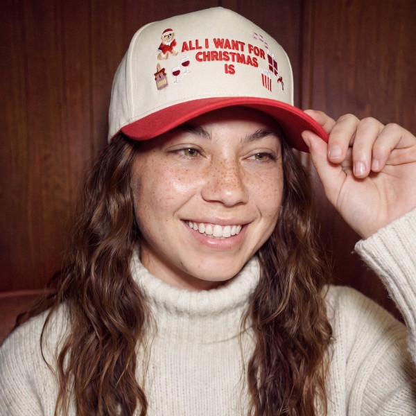 All I Want For Christmas Is Baseball Cap with playful embroidered lettering surrounded by wrapped presents and a sleepy Zzz, a cute nod to naps and gifts. A structured cap with a bold contrast brim that brightens up any cold weather outfit. Great for Christmas parties, holiday travel, tree lighting events, and matching family photos. Funny holiday phrase hats sell quickly as gifts and are an easy add on for any Christmas display.