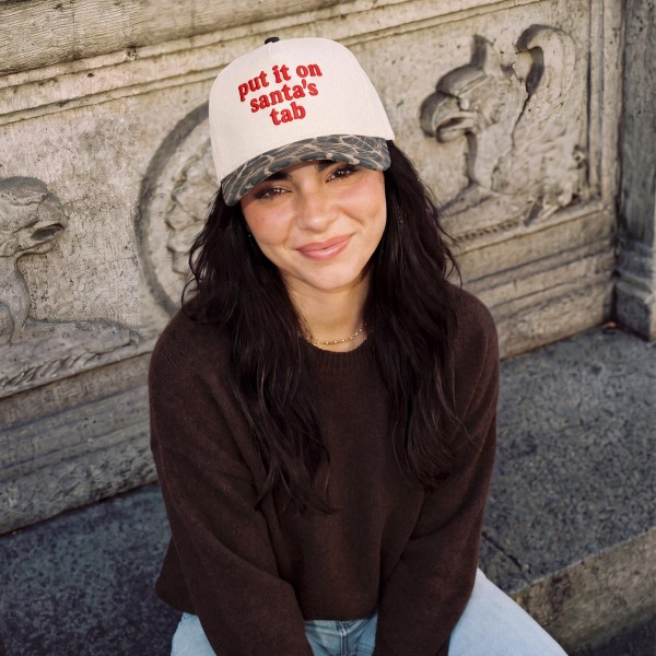 Put It On Santa's Tab Baseball Cap with cheeky embroidered script lettering across the front and a contrast brim for a fun holiday twist. A structured cap that tops off cozy sweaters, shackets, and leggings for an effortless festive look. A hit for holiday shopping sprees, Christmas parties, girls night out, and white elephant gift swaps. Funny Christmas sayings are always a top seller, making this cap an easy grab and go gift at checkout.