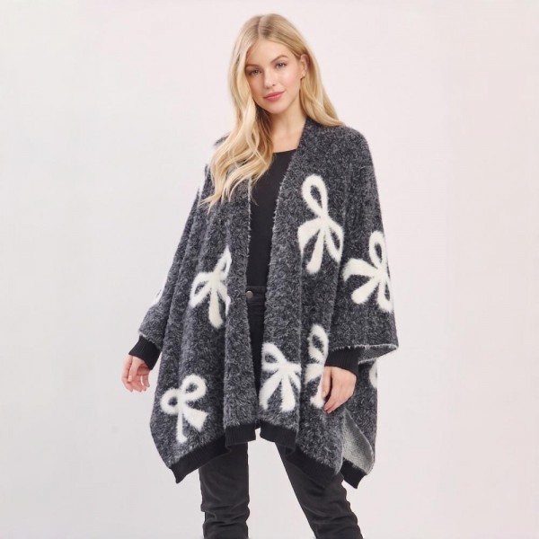 Bow Print Knit Ruana Poncho with an open-front drape and generously oversized fit. The double-sided jacquard knit showcases a whimsical allover bow motif with contrast edging — an easy one-size topper that layers beautifully over basics for an instant outfit. A playful statement piece with strong gift appeal that stands out on boutique racks and social feeds alike.