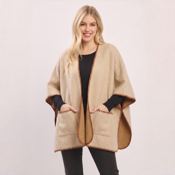 Open front ruana wrap in a brushed knit with patch pockets and contrast blanket stitch along every edge. One size drape falls past the hip, layers over a tee or a turtleneck, and throws on without fussing with buttons. A fall and winter layer for boutique buyers stocking travel, football weekends, church, and cold office mornings. Pocketed ruanas photograph well on a mannequin and sell as the piece that finishes the outfit.