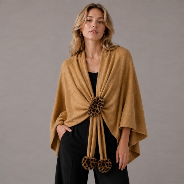 Knit cape wrap with faux fur pom ties at the front, cut wide enough to drape over the shoulders and fall past the hip. The soft brushed yarn feels substantial without weighing down a shoulder, and the open silhouette layers over almost anything on the rack. Sizing is forgiving, so one piece works across a wide customer range. A strong window piece that drives a higher ticket through fall and holiday.