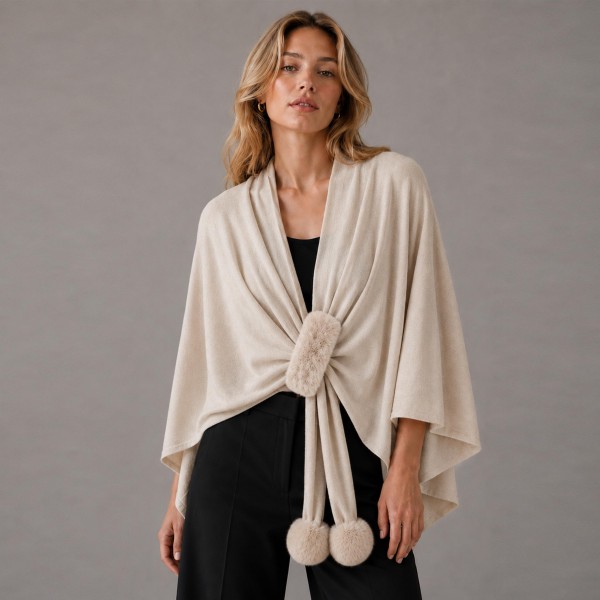 Knit cape wrap with a faux fur pom tie closure at the front, cut wide enough to drape over the shoulders and fall past the hip. The soft brushed yarn feels substantial without weighing down a shoulder, and the open silhouette layers over almost anything on the rack. Sizing is forgiving, so one piece works across a wide customer range. A strong window piece that drives a higher ticket through fall and holiday.