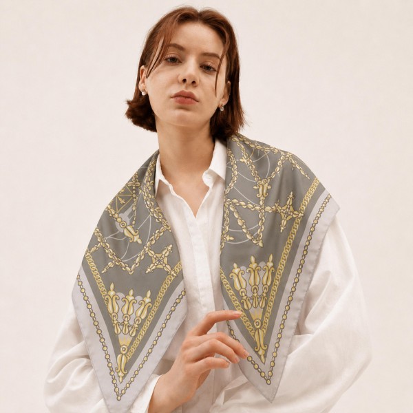 Chain and tassel print square scarf in a lightweight satin-feel woven, with an ornate link motif and a framing border. The generous square drapes over the shoulders like a shawl, folds into a neck knot, or ties onto a handbag for an instant lift. Status chain prints give a display an elevated, designer-inspired look at an impulse price point. A strong transitional piece that carries from early fall into holiday.