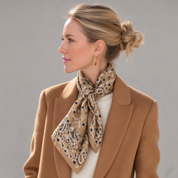 Paisley Bandana Print Square Scarf in silky 100% polyester, measuring 27.5 inches square. A classic bandana layout pairs a detailed paisley border with a medallion center. Knot it at the neck, wear it as a headscarf, or tie it onto a bag handle for an easy, laid back touch. A timeless print that layers well over sweaters and jackets, it is a dependable seller in every season.