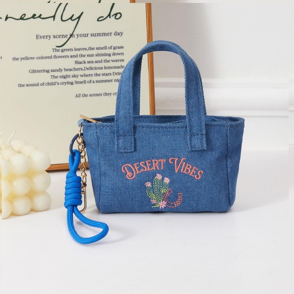 A boho-chic structured mini handbag in denim fabric featuring a hand-embroidered 'Desert Vibes' script and cactus motif, with a removable wrist strap for easy carry. The laid-back desert aesthetic resonates with free-spirited shoppers and pairs naturally with casual and festival fashion. Compact and boutique-ready, it drives impulse purchases when displayed near lifestyle accessories or summer apparel. A versatile seller with strong appeal across multiple customer demographics.