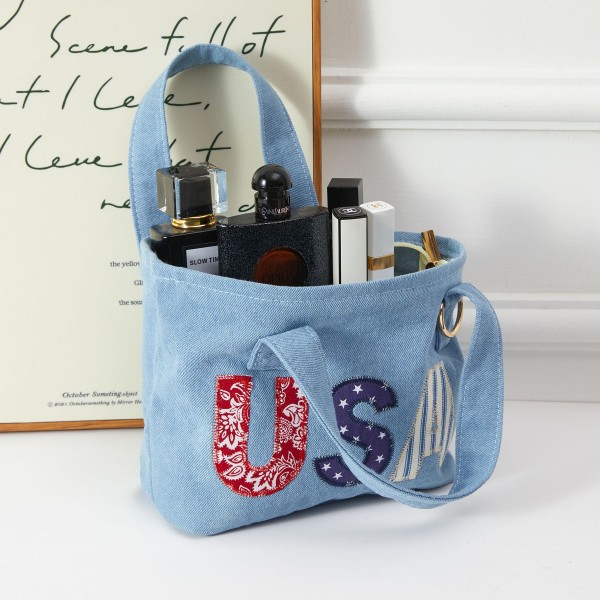 A patriotic denim mini tote featuring bold 'USA' applique letters in stars-and-stripes fabric, finished with a metal ring accent. Sturdy construction and comfortable top handles make it practical for everyday use while delivering strong seasonal appeal around summer holidays. A natural add-on for boutiques building Fourth of July and Memorial Day merchandise displays, it appeals to patriotic shoppers and functions equally well as a gift item or impulse buy.