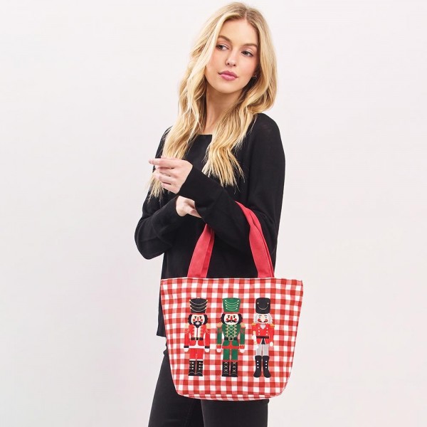 Gingham canvas tote with an embroidered nutcracker trio and contrast webbing handles. Roomy open top carries a wrapped gift, a bottle of wine, or a stack of cookies to the party, and the flat base keeps it upright on a counter. A seasonal carry for boutique buyers stocking hostess gifts, teacher gifts, cookie exchanges, and holiday markets. Embroidered gingham totes double as the gift and the wrapping, which is why they sell out every December.