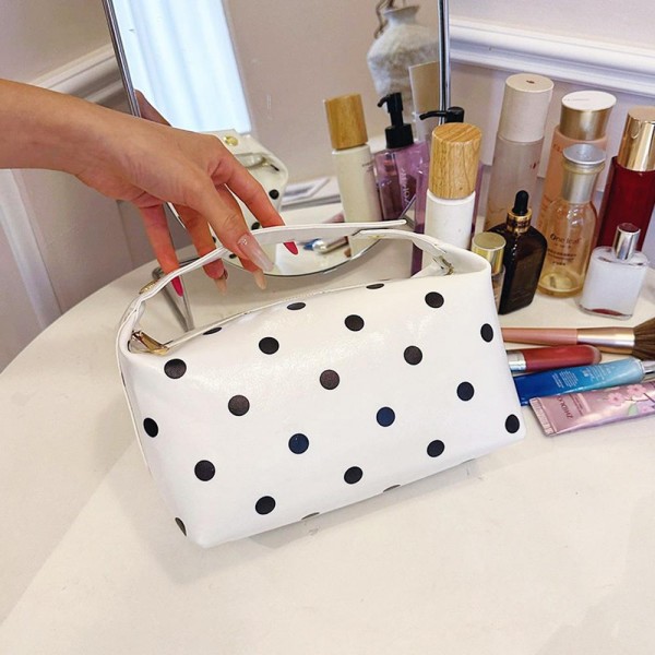 Coated polka dot cosmetic bag with a wide curved zip opening and a soft structured body that keeps its shape when full. Deep enough to stand brushes upright with room left for bottles laid flat. The wipe clean shell shrugs off powder and spills, so it still looks new after a season of daily use. A pretty, practical piece that sells on its own and sells better beside a matching tote.