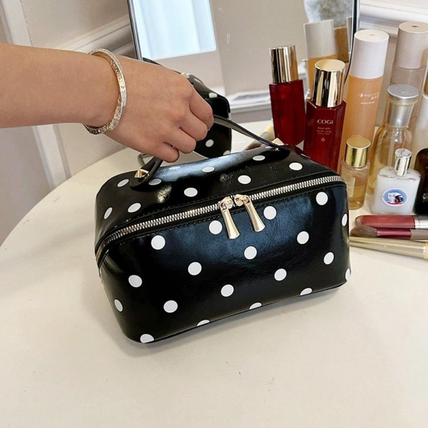 Wide opening makeup case that unzips almost fully so everything lies flat and visible instead of buried at the bottom. A padded body protects glass bottles and pressed compacts, and the short top handle makes it easy to move from counter to suitcase. The coated polka dot exterior wipes clean with a damp cloth. An everyday travel piece priced for repeat purchase and easy gifting.